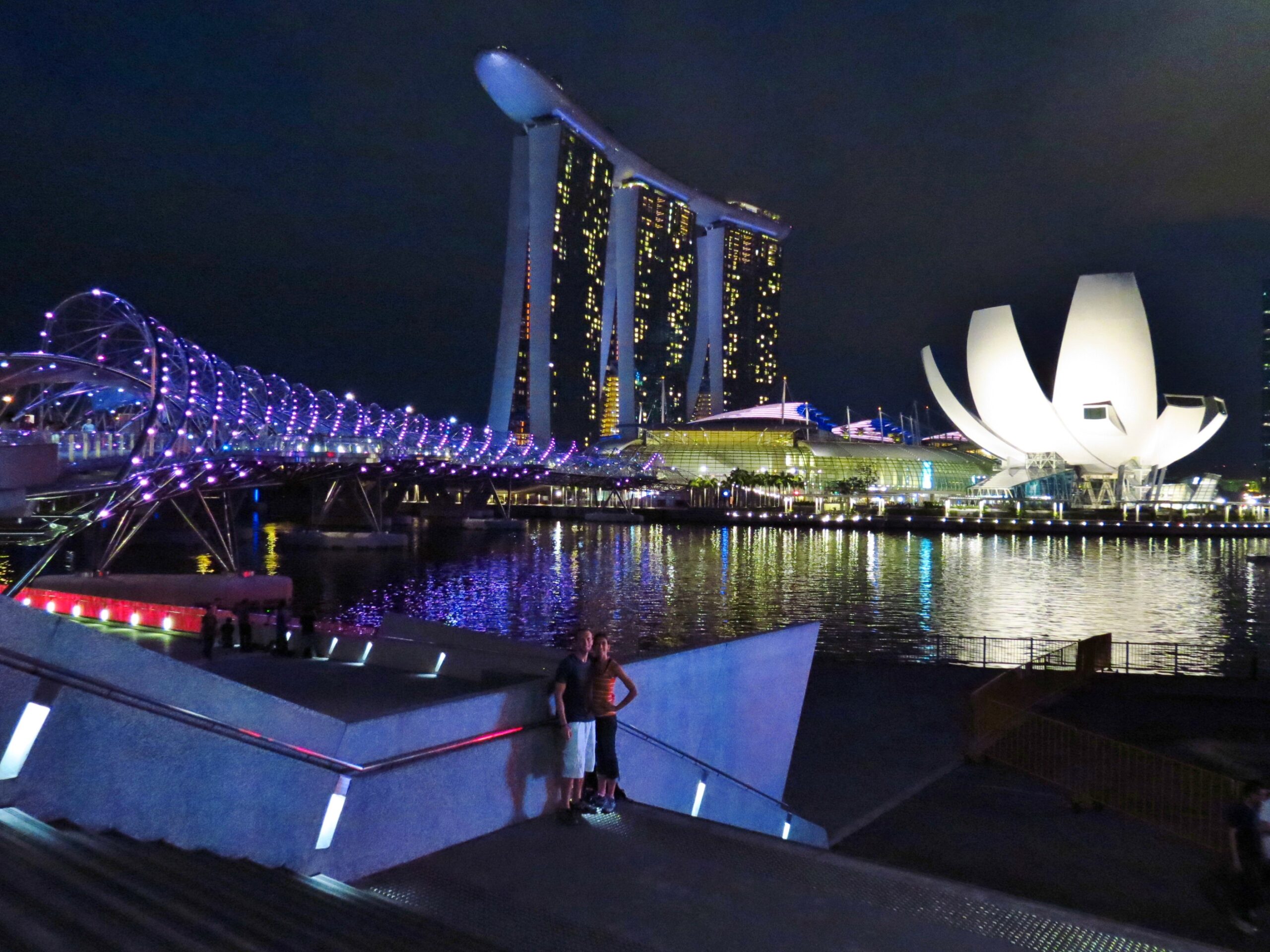 A couple standing in front of the Helix Bridge and Marina Bay Sands Hotel in Singapore at night