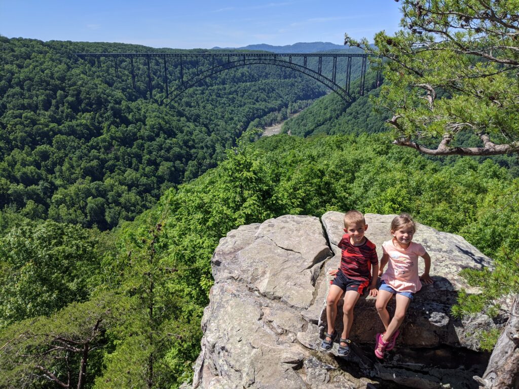 Two young children sitting on a rock with a large bridge in the background