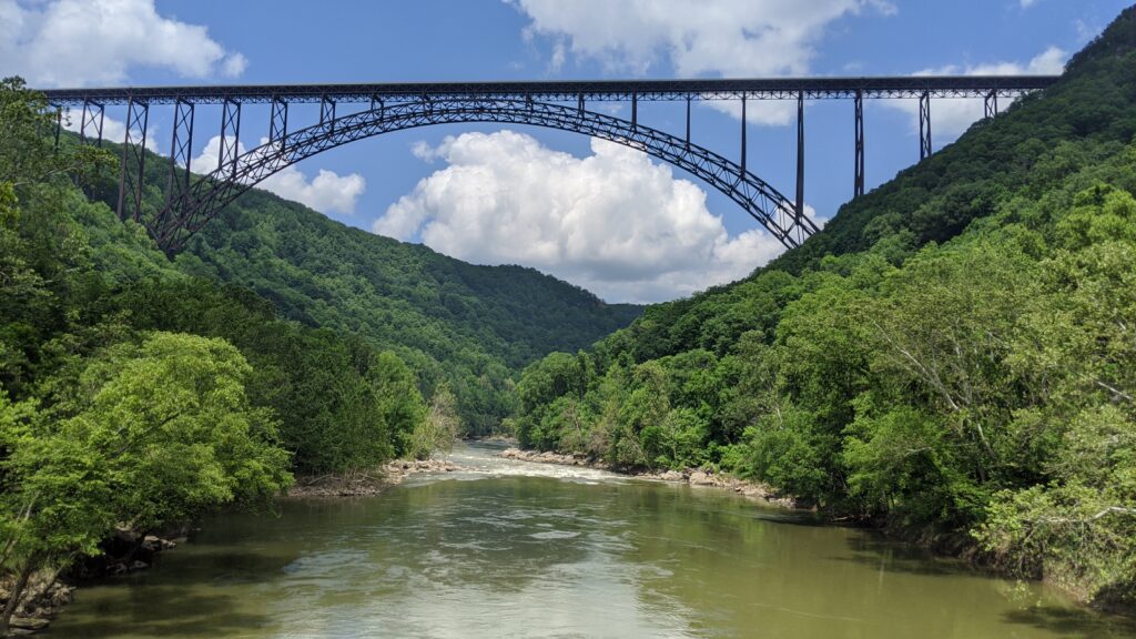 A high steel bridge over a river with blue sky and clouds in the background