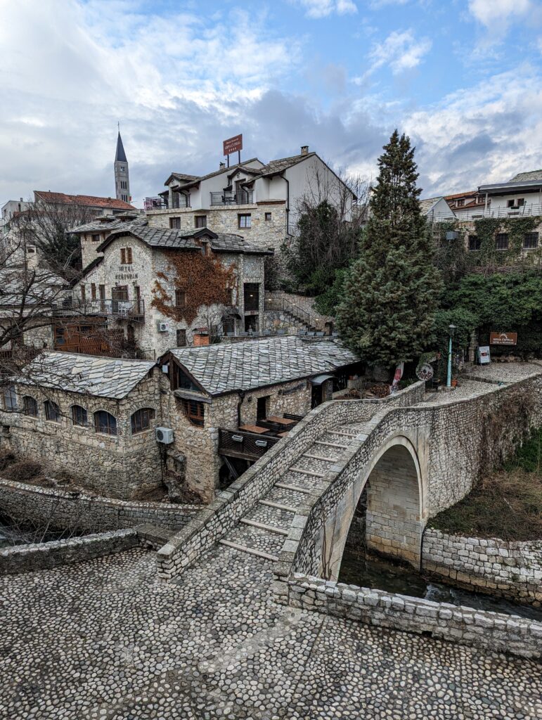 A small stone bridge with stone buildings in the background in Mostar