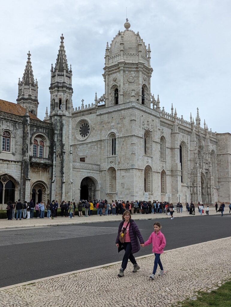 A woman and girl holding hands walking in front of the Jeronimos Monastery in Lisbon, Portugal
