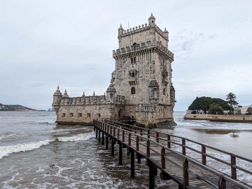 An empty wooden bridge leading over water to the stone Tower of Belem in Lisbon