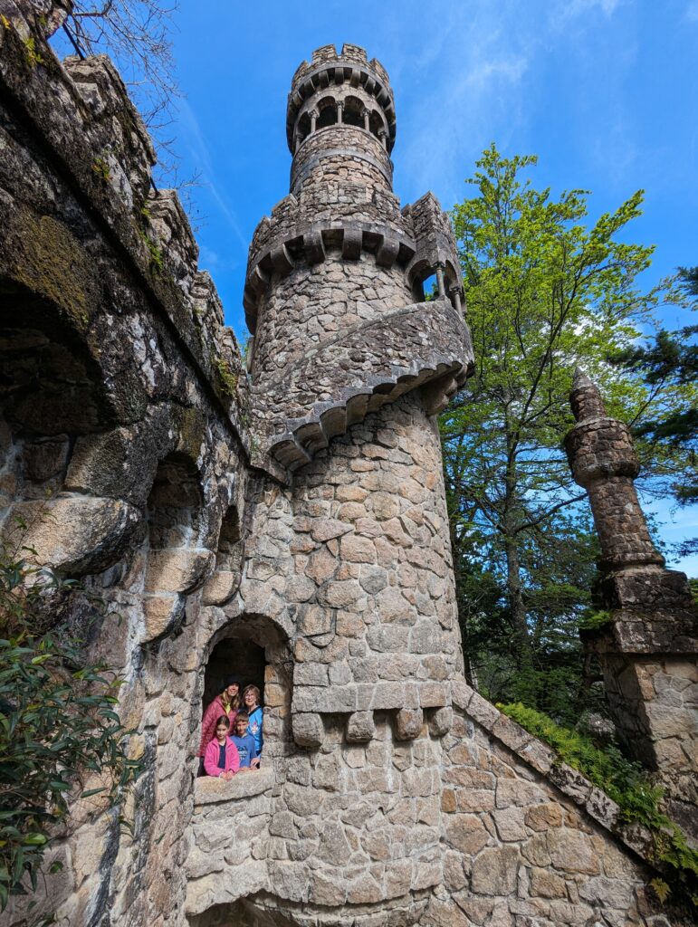 A family framed in a stone arch with a large tower above them in Quinta da Regaleira
