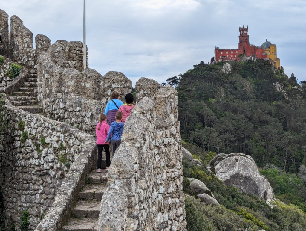 A group ascending a stone staircase with a colorful Pena Palace atop a hill in the background