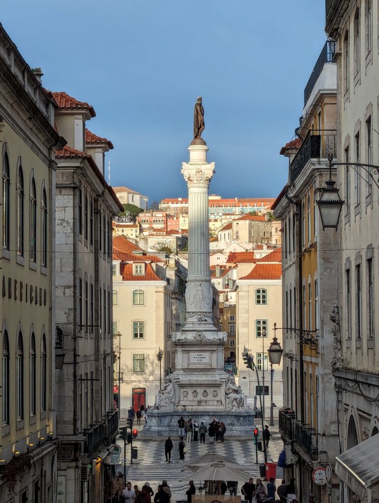 A dark statue atop a tall, white column in Lisbon, Portugal
