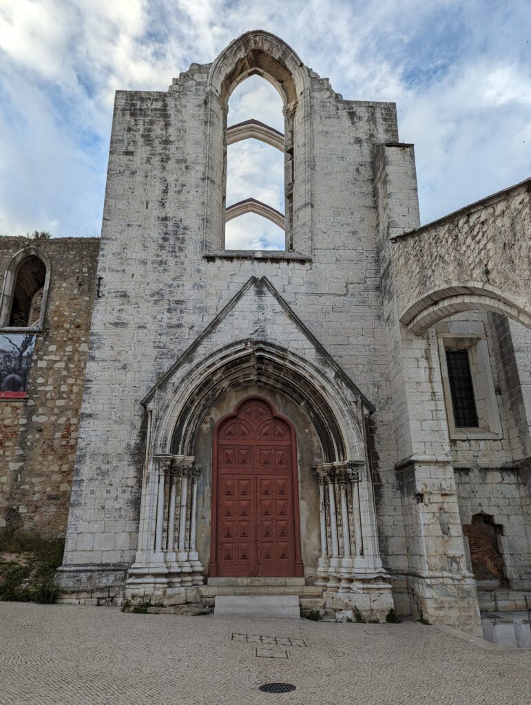 A big wooden door below stone arches at the Carmo Convent in Lisbon, Portugal
