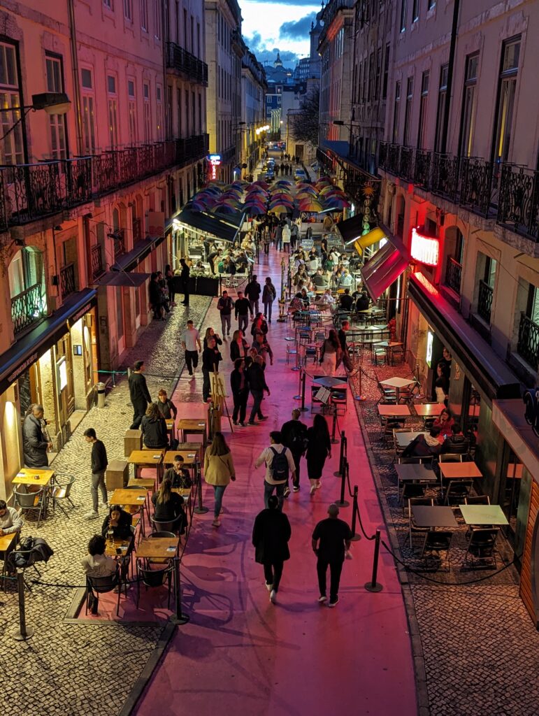 An elevated view of a crowded pink street in Lisbon, Portugal with lots of people and tables