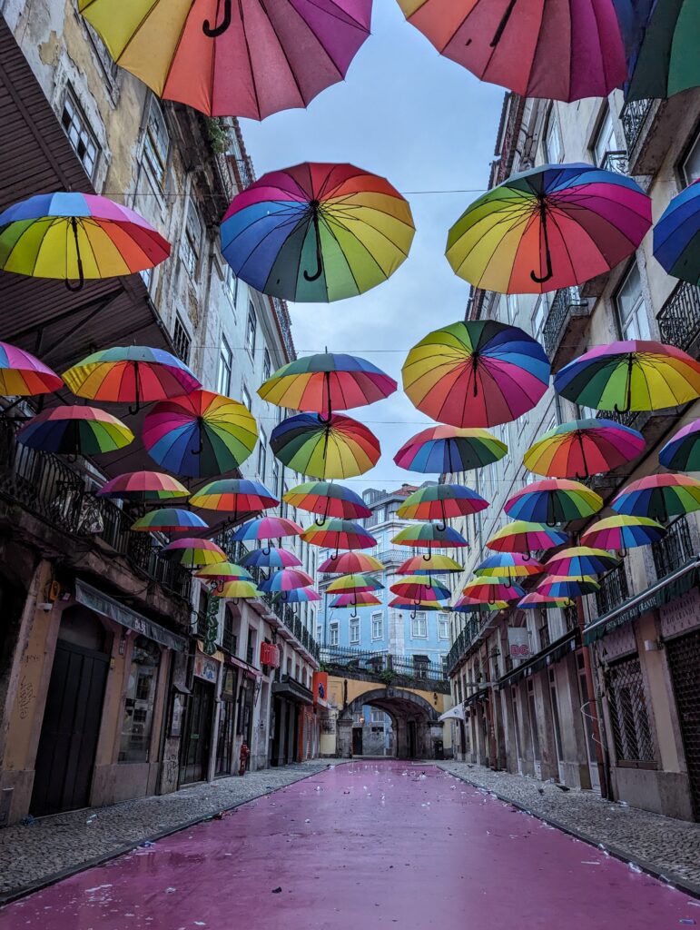 Colorful umbrellas hanging above a pink street in Lisbon, Portugal