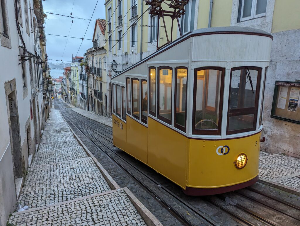 A yellow and white street car at the top of the Elevador da Bica in Lisbon, Portugal