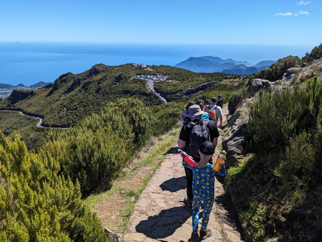 A group of hikers on a stone path with a parking lot and hills in the distance