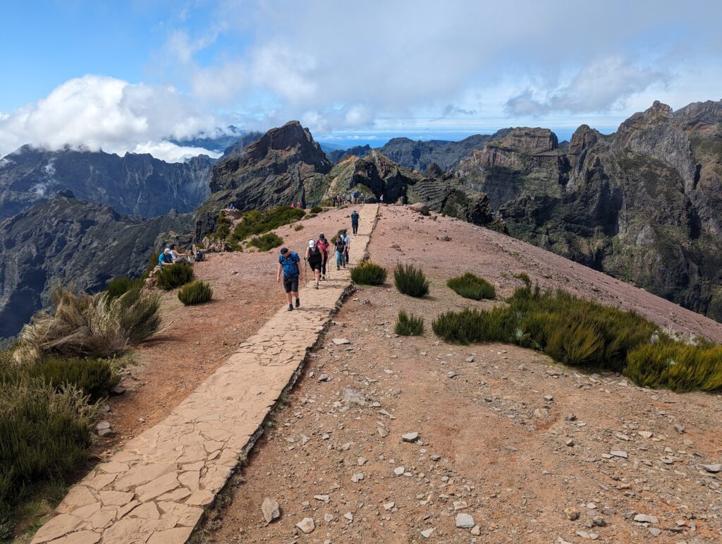 Multiple people walking along a stone path with mountains and clouds in the background