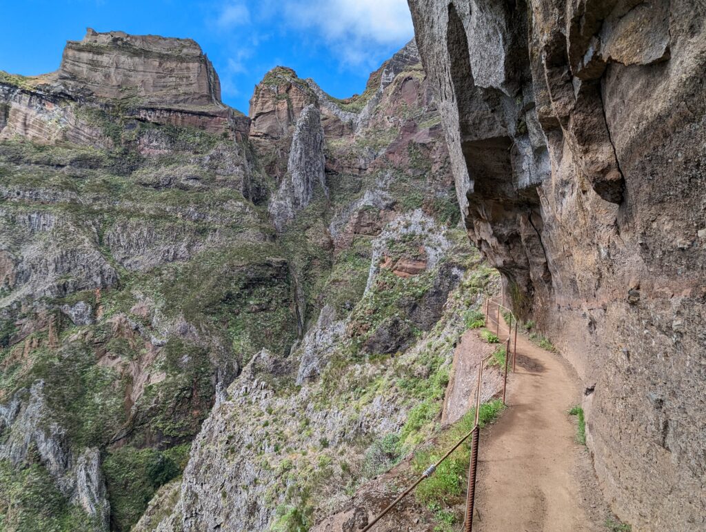 A narrow trail along a rock wall with mountains in the background