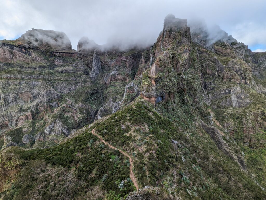 A green and rocky mountain landscape with clouds at the top