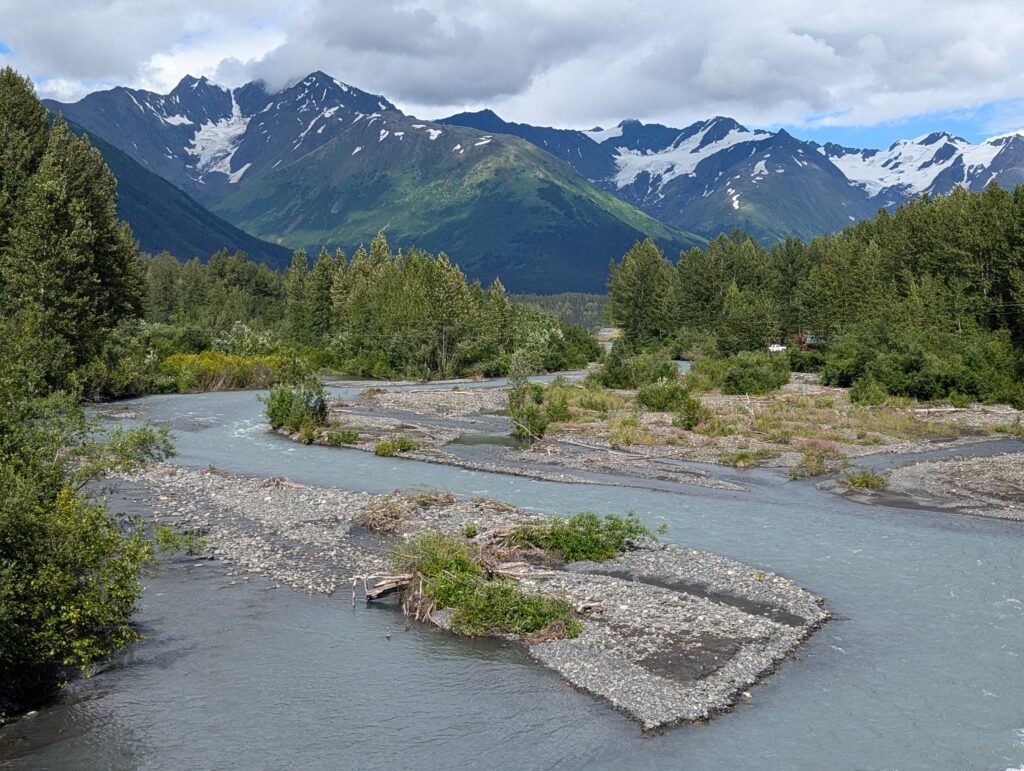 Snow covered mountains and clouds with a winding river in the foreground