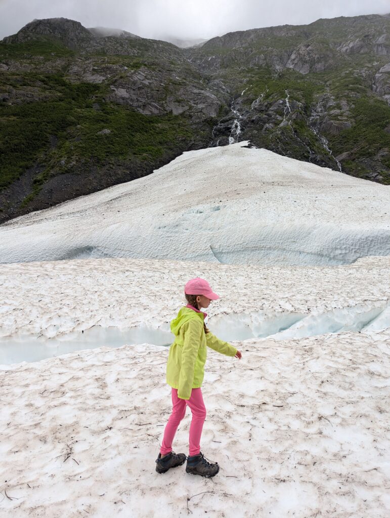 A girl walking on snow with a cloudy mountaintop in the background