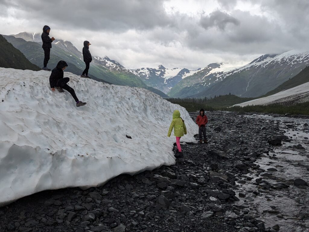 Several children playing on snow with mountains lining the entire background