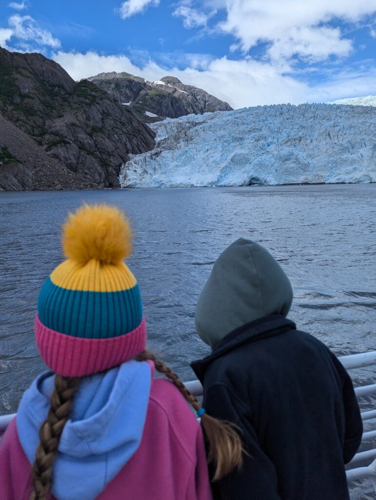 The backs of two children looking at a glacier while on a boat in Alaska