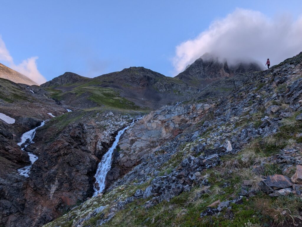 The silhouette of a person at the top of a mountain with a waterfall further down