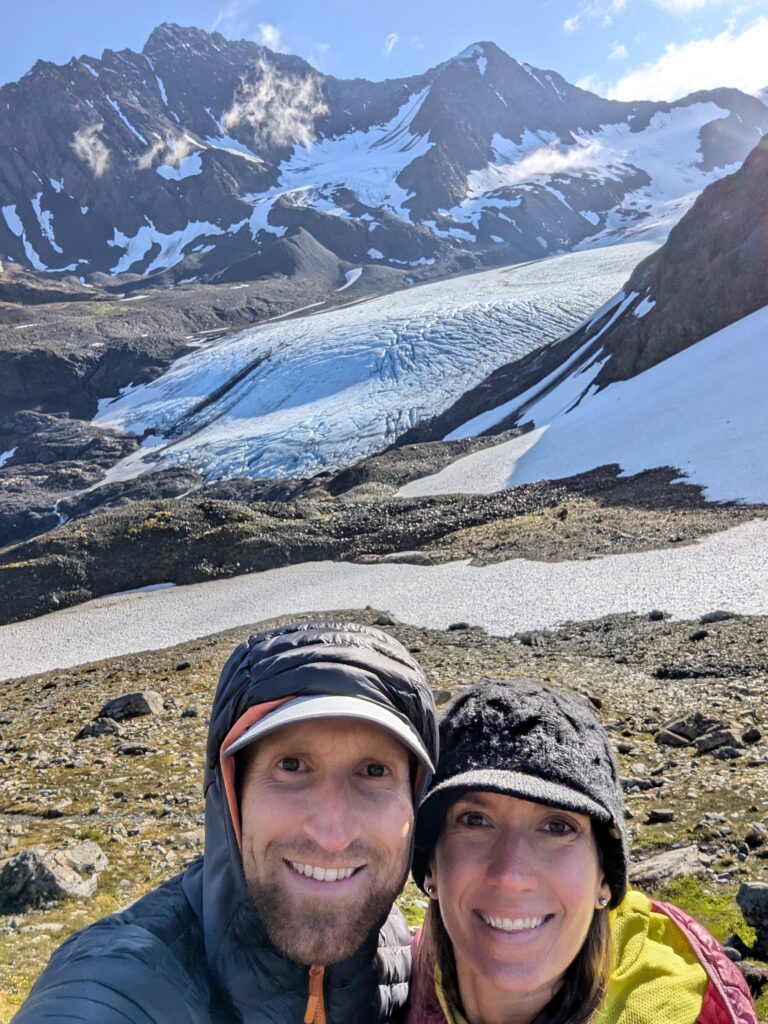 A couple in front of Raven Glacier and jagged mountains in Alaska