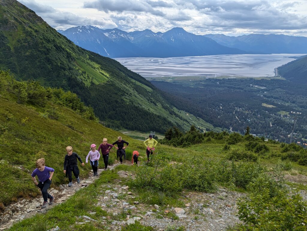 A group walking on a stone trail through grass with a body of water and mountains far off in the distance