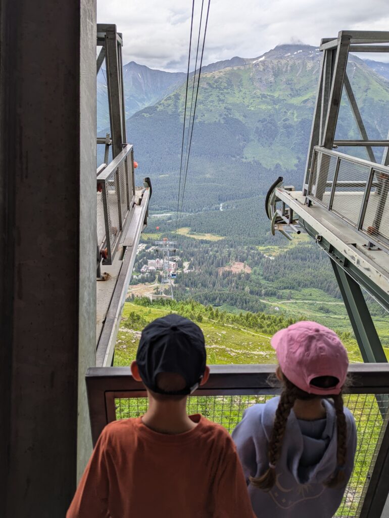 The backs of two children looking down a platform at a distant Alyeska resort far below