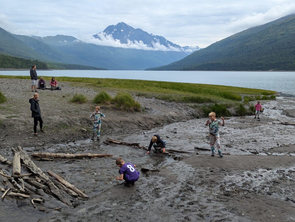 Children playing in shallow water leading to Eklutna Lake with a prominent mountain peak in the background