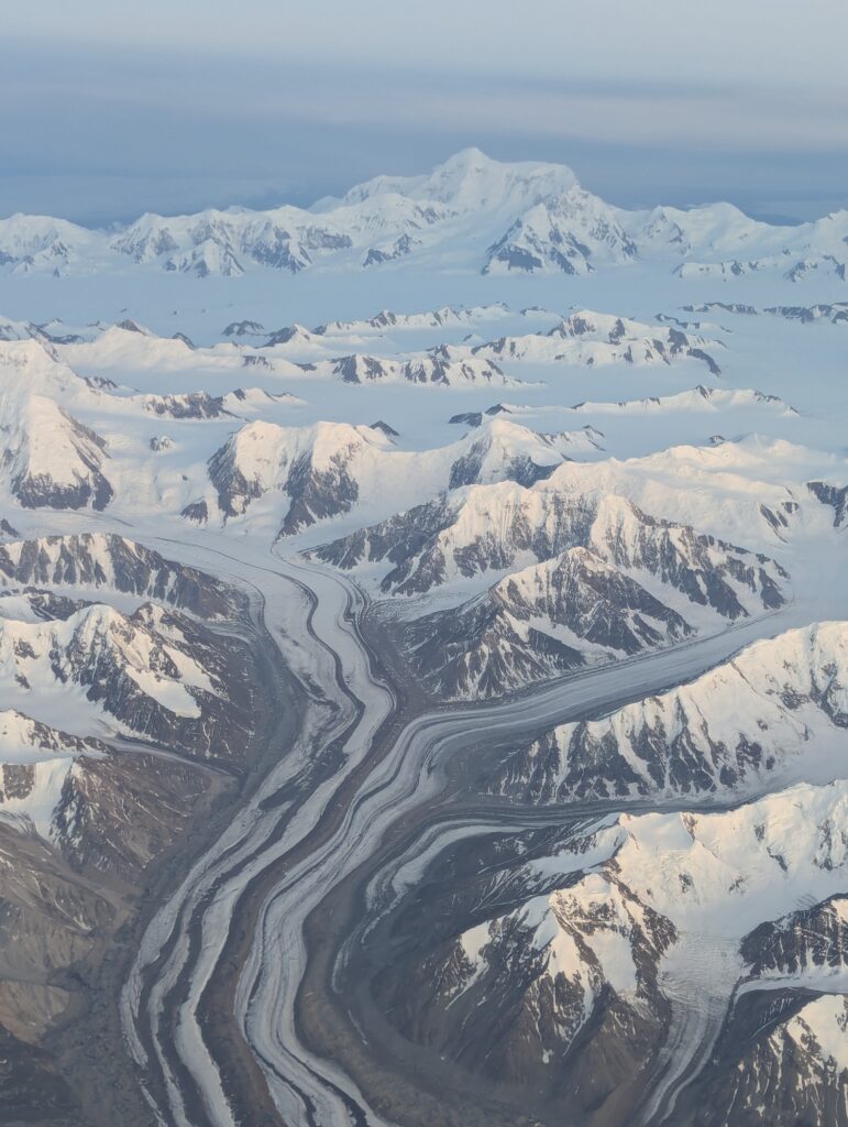 A hazy view of snowy mountain peaks from an airplane over Alaska