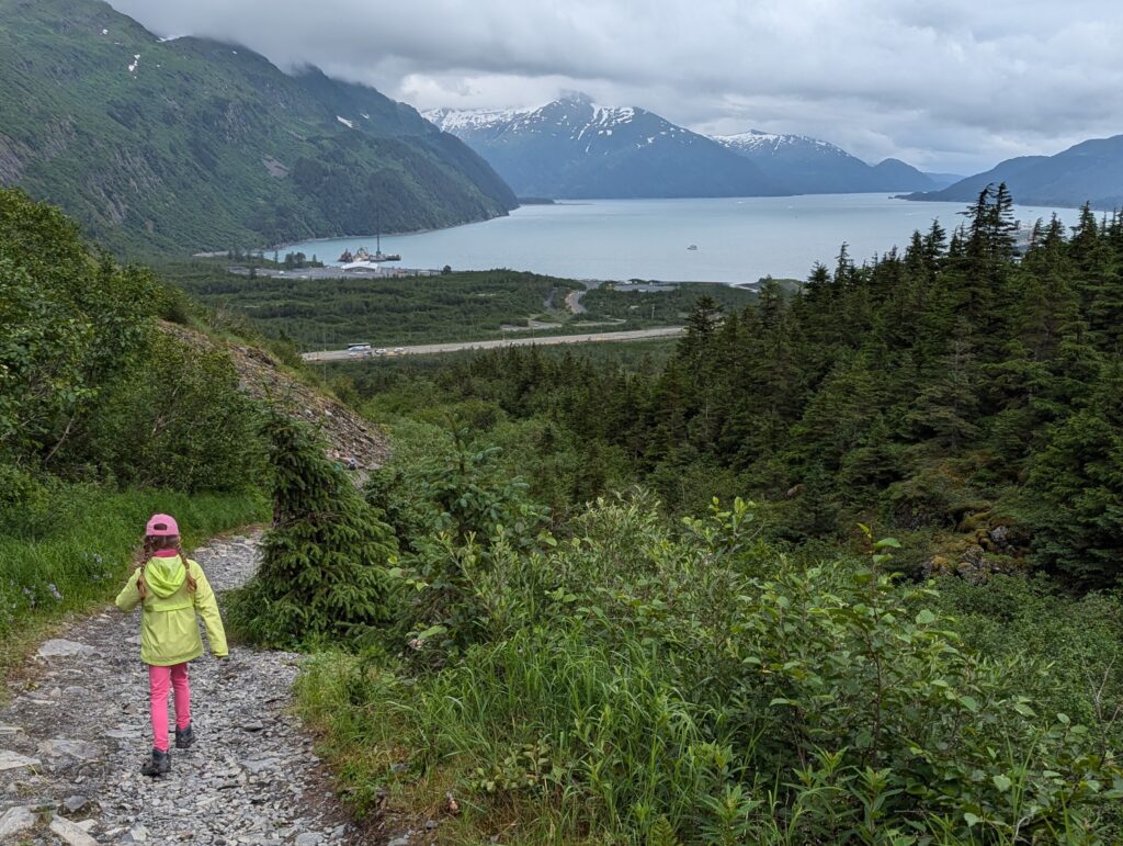 A young girl walking along a stone path with a lake and snow covered mountains far away