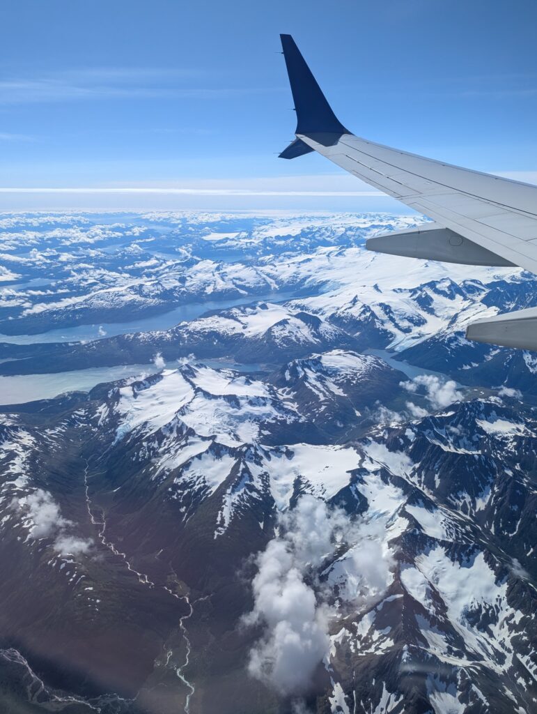 An airplane wing, snow-covered mountains, and rivers as seen when flying over Alaska