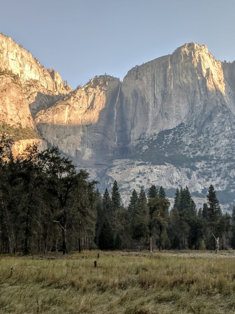 A low-flowing Yosemite Falls with trees and a meadow in the foreground