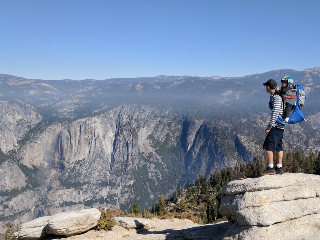 A man with a child in a backpack overlooks Yosemite Falls 