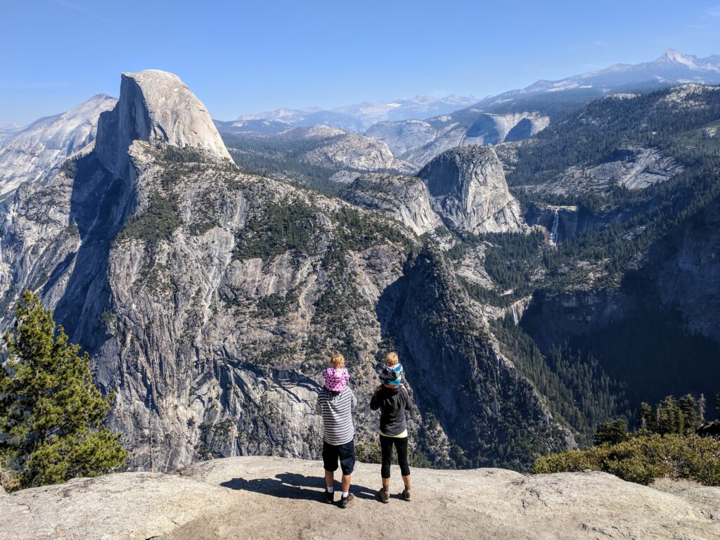 A couple with children on their shoulders looking at Half Dome from Glacier Point