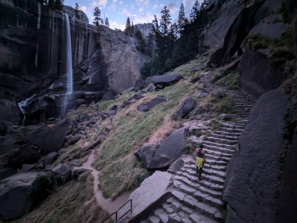 A woman standing on stone stairs looking at a waterfall in Yosemite