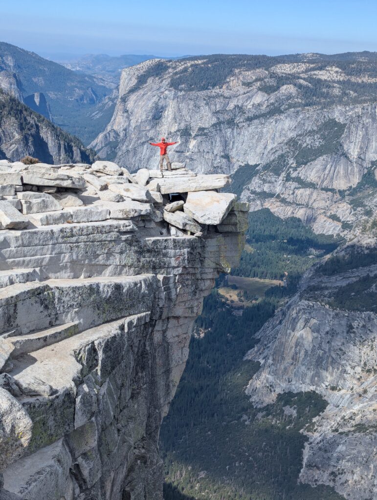 A hiker stands on an outcropping of rocks with a long drop below