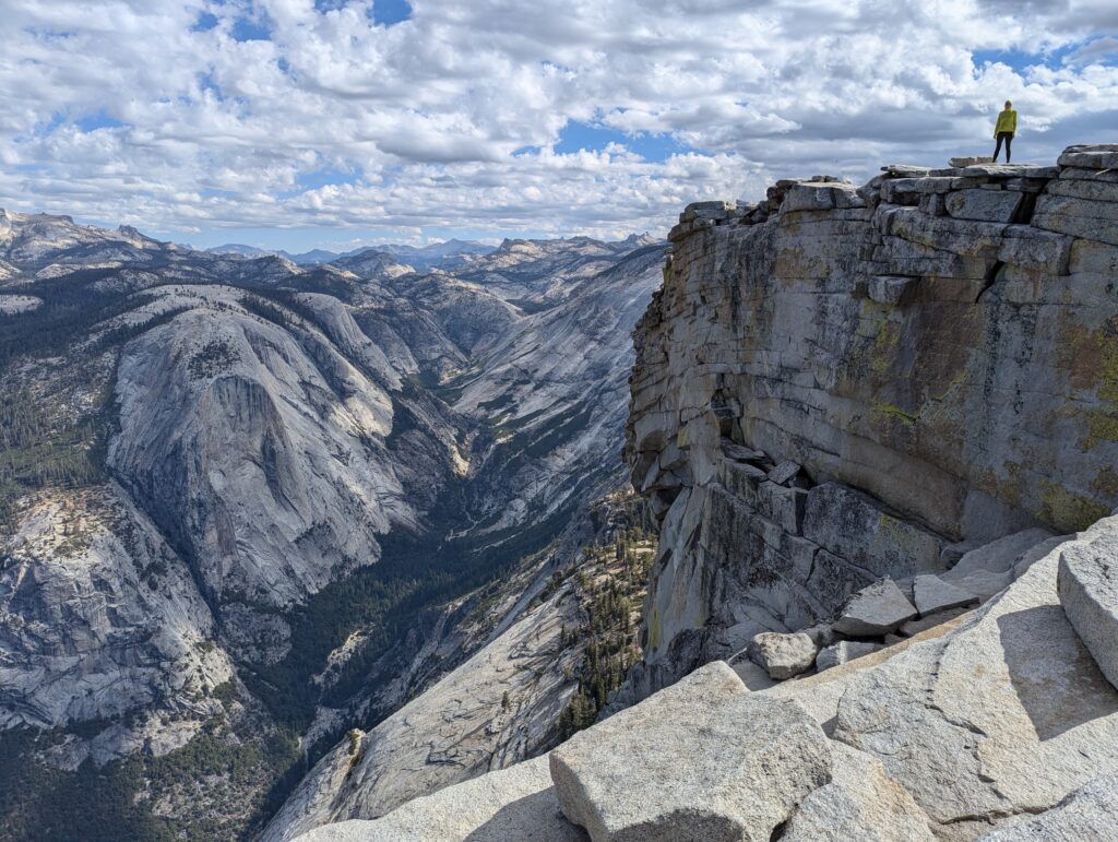 A person standing atop rocks with clouds in the background and mountains stretching in the horizon